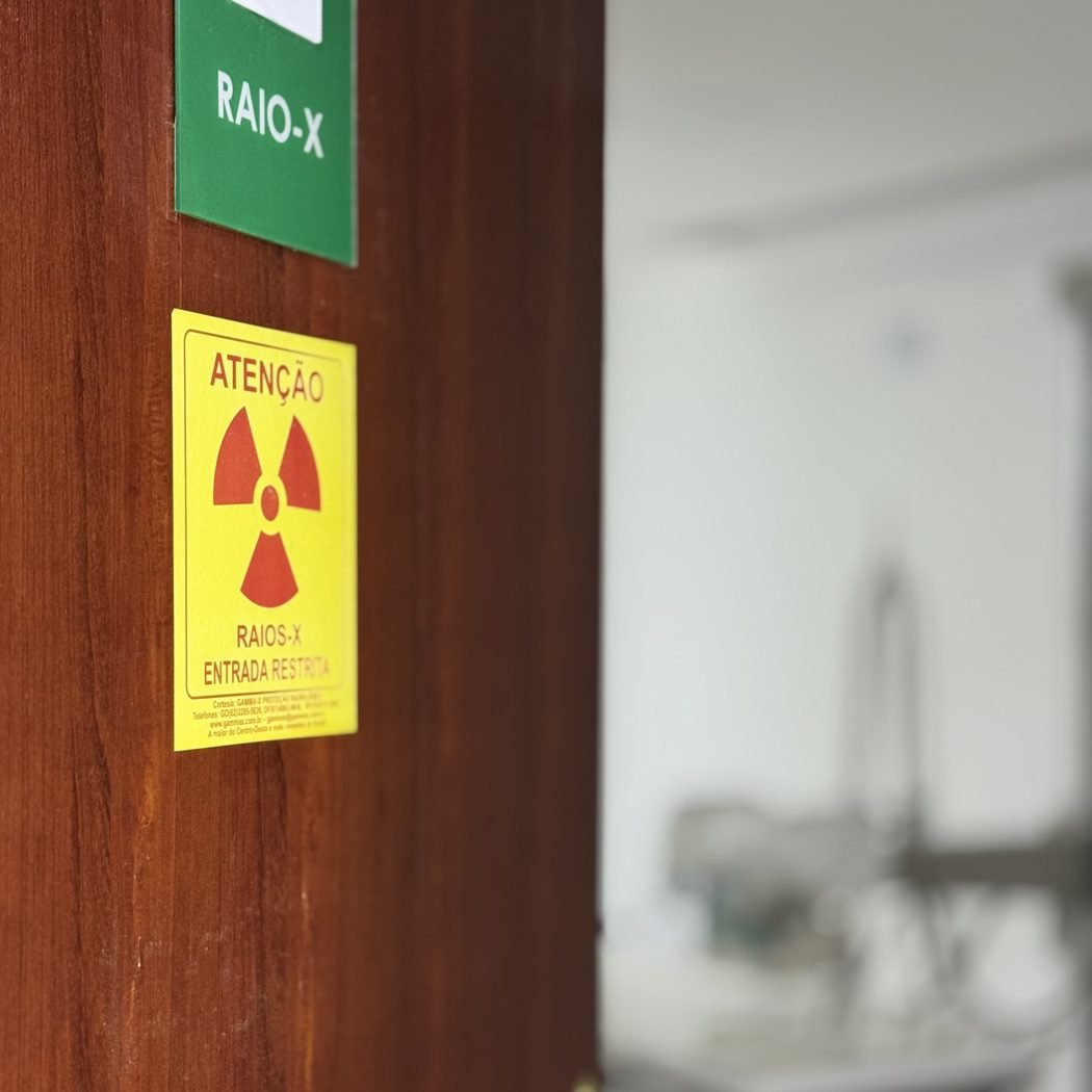 Porta da sala de raio-x do Centro Médico NEXO, com a placa e o aviso de radiação